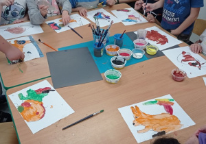Dzieci siedzą przy stoliku i malują farbami zwierzątka