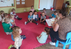 Dzieci siedzą na dywanie i słuchają bajki pt. "Czerwony Kapturek". którą czyta zaproszony Rodzic