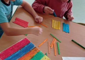 Chłopiec z dziewczynką układają kolorowe patyczki w odpowiednie miejsce w pudełku