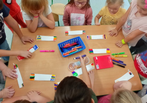 Dzieci siedzą przy stole i robią kolorowe tęcze mazakami