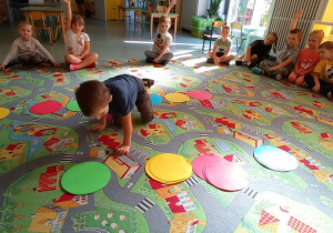 Dzieci siedzą na dywanie i układają kolorowe koła wg wzoru