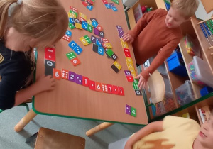 Dzieci siedzą przy stole i układają domino matematyczne