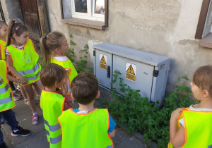 Dzieci stoją przed skrzynką elektryczną i omaiają znalezione na niej znaki