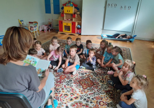 Dzieci siedzą na dywanie, Pani Agnieszka czyta książeczkę o przygodach czterech piesków