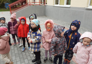 Dzieci stoją na tarasie i słuchają o opiece nad alpakami
