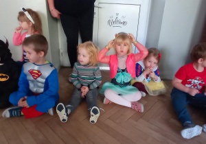 Dzieci siedzą na podłodze i słuchają zagadek Minionka