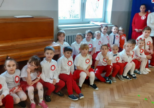 Zdjęcie grupowe "Biedronek". Dzieci siedzą na ławeczkach w biało-czerwonych strojach