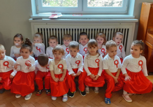 Zdjęcie grupowe "Zajączków". Dzieci siedzą na ławeczkach w biało-czerwonych strojach