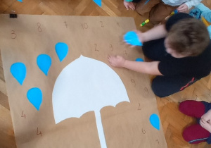 Dzieci naklejają kropelki w odpowiednim miejscu na dużym plakacie z parasolką