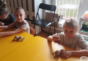 Dzieci siedzą przy stoliku i malują farbami kawałek platonki po jajkach