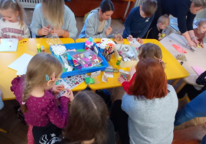 Dzieci z bliskimi siedzą przy stole i wykonują ozdoby świąteczne