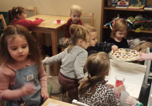 Dzieci siedzą przy stoliku, częstują się ciasteczkami.