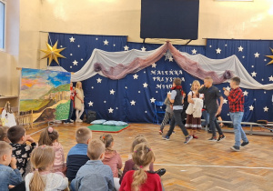 Na scenie aktorzy w przedstawieniu "Królowa Śniegu", dzieci siedzą i oglądają występ.