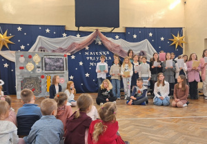 Dzieci słuchają kolęd śpiewanych przez uczniów ze szkolnego chóru.