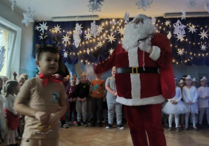 Mikołaj na scenie rozmawia z dzieckiem w stroju renifera.