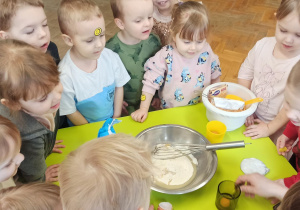 Dzieci stoją przy stoliku na którym jest miska ze składnikami na pączusie
