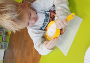 Chłopiec siedzi przy stoliku i posypuje cukrem pudrem swojego pączusia