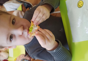 Chłopiec siedzi przy stoliku i ze smakiem zjada małego pączusia