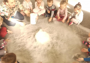 Dzieci siedzą w kole na dywanie w obłoku z suchego lodu