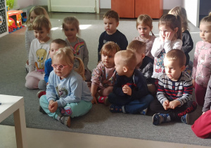 Dzieci siedzą na dywanie i z zaciekawieniem obserwują eksperyment