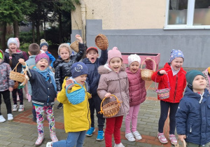 Dzieci z grupy III stoja z koszyczkami gotowe na zbieranie jajeczek w ogrodzie przedszkolnym