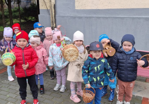 Dzieci z grupy I stoja z koszyczkami gotowe na zbieranie jajeczek w ogrodzie przedszkolnym