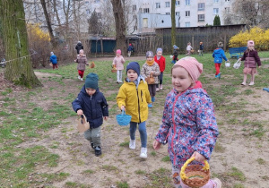 Dzieci biegaja po ogrodzie i szukają jajeczek od Zajączka Wielkanocnego