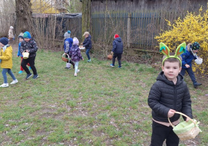 zDzieci biegaja po ogrodzie i szukają jajeczek od Zajączka Wielkanocnego