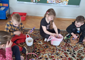 Dzieci siedzą na dywanie i oglądają w swoich koszyczkach słodycze od Zajączka Wielkanocnego