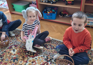 Dzieci siedzą na dywanie i oglądają w swoich koszyczkach słodycze od Zajączka Wielkanocnego