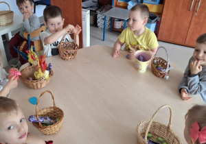 Dzieci siedzą przy stoliczkach i oglądają w swoich koszyczkach słodycze od Zajączka Wielkanocnego