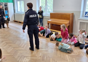 Policjanci uczą dzieci pozycji "żółwia" w obecności psa policyjnego