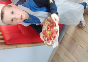 Chłopiec niesie talerz z przygotowanę przez siebie pizzą do pieca