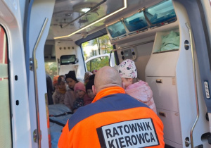 Dzieci oglądają w środku ambulans, Ratownik Medyczny odpowiada na każde pytanie i opowiada dzieciom o wyposażeniu