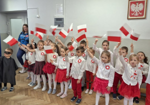 Dzieci śpiewają piosenkę i trzymają flagi wysoko uniesione w górę