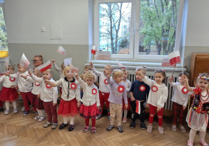 Dzieci śpiewają piosenkę i tzrymają w dłoni flagi wysoko uniesione w górę