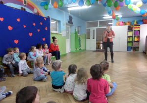 Dzieci siedzą na podłodze i słuchają piosenki z musicalu "Anastazja" Śpiewanej przez prowadzącą.