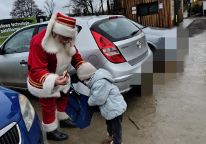 Mikołaj wita kolejno każde dziecko i częstuje niespodzianką z torby