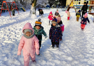 Dzieci w ogrodzie zasypanym śniegiem chodzą robiąc ślady swoich butów