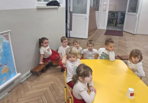 Wybrani reprezentanci grupy siedzą przy stoliku, przy nich na ławeczce siedzą ich koledzy