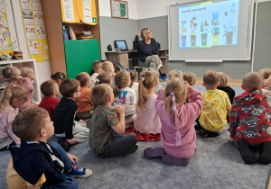 Dzieci siedzą na dywanie, oglądają multimedialną dotyczącą prawidłowej segregacji śmieci