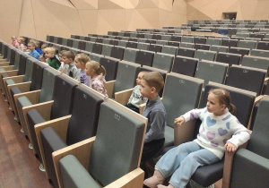 Dzieci siedzą w sali i czekają  na koncert