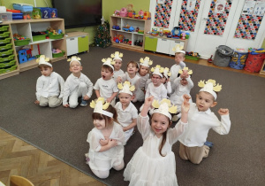 Dzieci radośnie siedzą na dywanie w strojach Aniołków