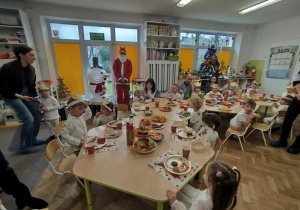 Dzieci razem z rodzicami siedzą przy stołach na których jest poczęstunek