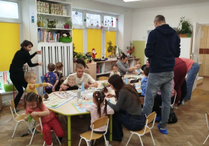 Rodzice z dziećmi siedzą przy stolikach z materiałami do tworzenia ozdób świątecznych