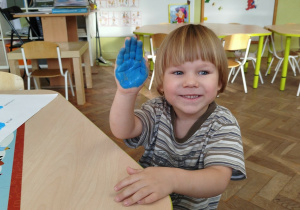 Uśmiechnięty chłopiec pokazuje swoją dłoń pomalowaną na niebiesko