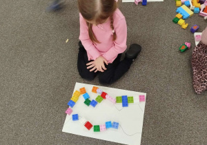 Dziewczynka układa klocki na kartce według wzoru