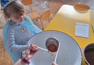 Dziecko trzyma klucz, nauczycielka leje wosk przez dziurkę