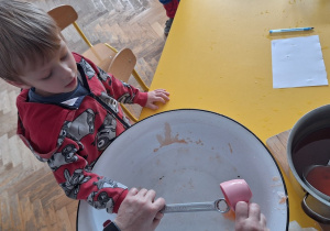 Dziecko trzyma klucz, nauczycielka leje wosk przez dziurkę