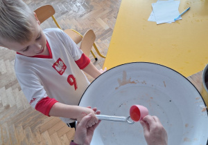 Dziecko trzyma klucz, nauczycielka leje wosk przez dziurkę